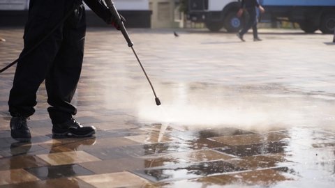 Cleaning city streets with water pressure washer. Janitor sprays city street sidewalk paving slabs. Worker disinfects floor and surfaces from coronavirus. Antibacterial sanitary measures on quarantine