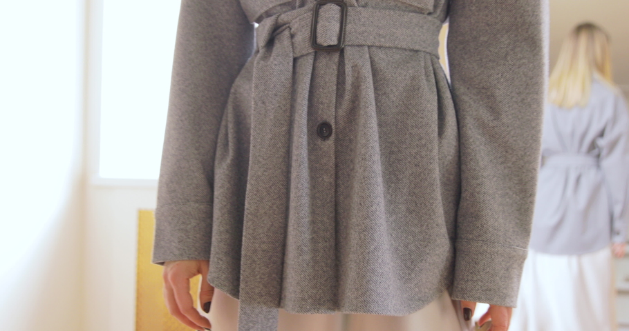 Blonde Woman Trying On The Woolen Grey Jacket With Belt In Front Of The Mirror Close-Up