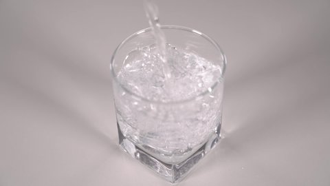Studio shot of water pouring into transparent glass on white table. Super slow motion.