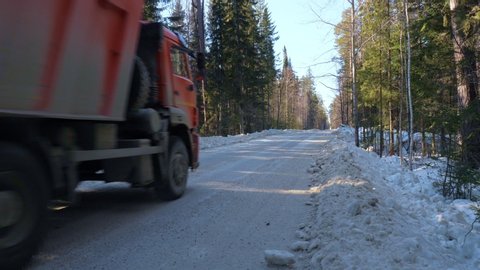 A truck carrying ore rides along a narrow winter forest road. The concept of labor and heavy industry