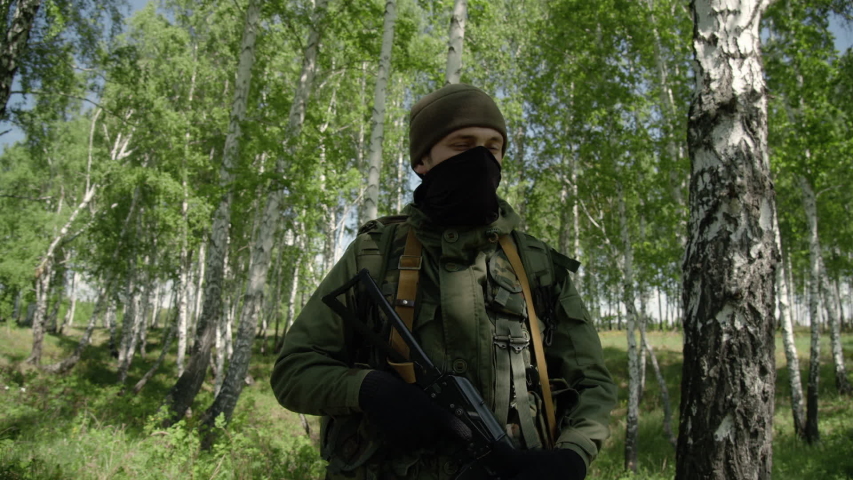 A soldier with a rifle stands in the forest