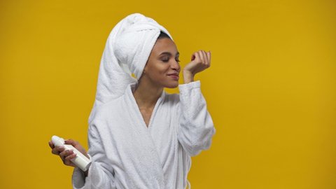 african american girl spraying deodorant isolated on yellow