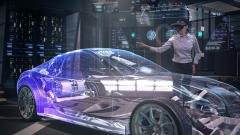 Automotive Female Professional Engineer wearing Futuristic Augmented Reality Headset redesigns Electric Car Prototype using Holographic Technology. High-tech facility. Electric car chassis.