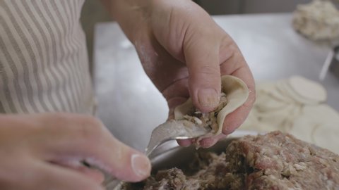 Close up of chef cook hands making dumplings with meat in commercial kitchen. Cook preparing traditional dumplings, gedza or khinkali in restaurant