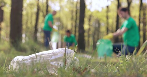 Volunteers in green T-shirts clean up the plastic trash in the park, shooting from a lower angle.