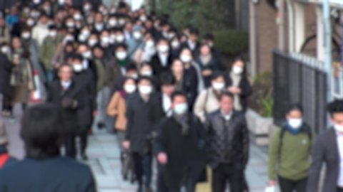 TOKYO, JAPAN -MARCH 2020 : Crowd of people walking down the street in morning rush hour. Many commuters going to work. People wearing mask to protect from Coronavirus(COVID-19) or cold. Blurred shot.
