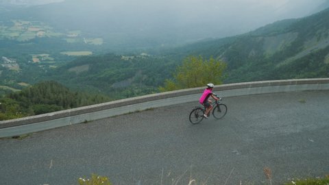 Biker in pink t-shirt makes a turn on mountain road, biking Tour de France route. Sportsman drive a bike on empty highway high in Alps