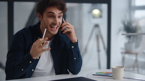 Closeup cheerful businessman talking mobile phone emotionally at home office. Positive entrepreneur supporting client on smartphone in slow motion. Happy business man finishing phone call indoor.