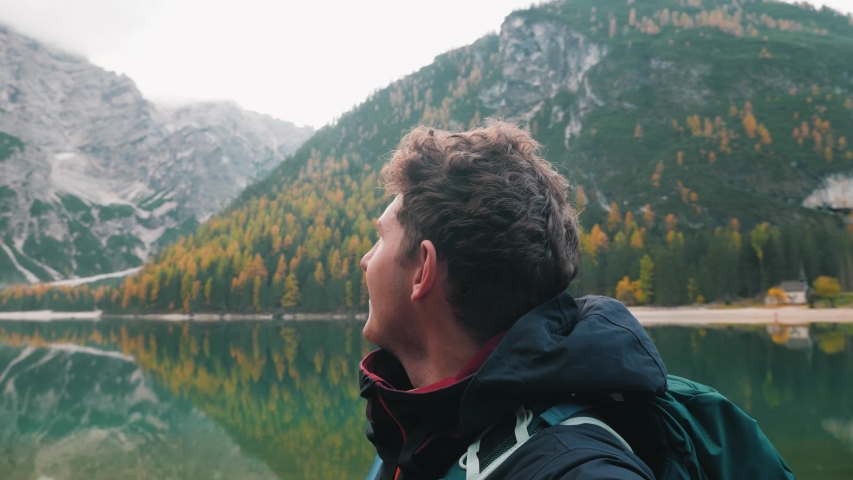 Adventurous caucasian man traveler hiking and enjoying nature at a peaceful alpine lake in the Dolomite mountains of Italy SLOW MOTION.