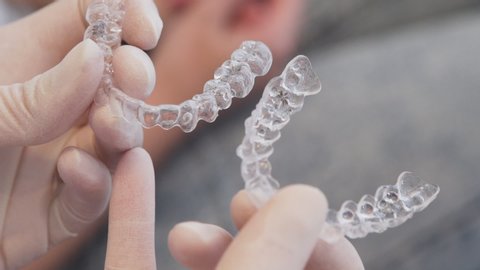 tight close-up of orthodontist putting two invisalign aligners side by side, with patient in the background