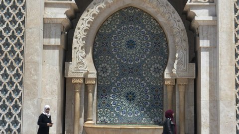 CASABLANCA, MOROCCO- JUNE, 9, 2019: two muslim women walk past an ablution fountain at hassan ii mosque in casablanca, morroco