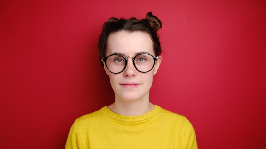 Lucky triumphing woman in eyeglasses celebrates amazing victory with both clenched fists, rejoices over awesome achievement, exclaims positively hooray, wears sweater, isolated over red background