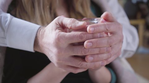 Close-up of senior male Caucasian hands caressing young female palms holding tea cup. Unity of couple with age difference. Leisure, lifestyle, love, romance.