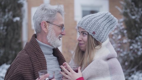 Portrait of Caucasian couple with age difference looking at each other with love and smiling at camera. Happy senior man and young woman posing outdoors on winter day. Love, age gap, lifestyle.