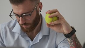 A close-up view of a handsome young businessman is holding a tennis ball during his work over white wall