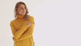 Displeased pretty blonde woman in sweater pointing at copyspace and disagreeing with something over grey background