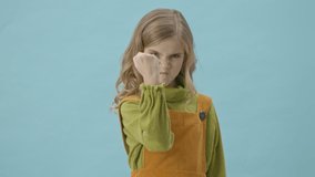 Angry little girl Showing fist to the camera isolated over blue background