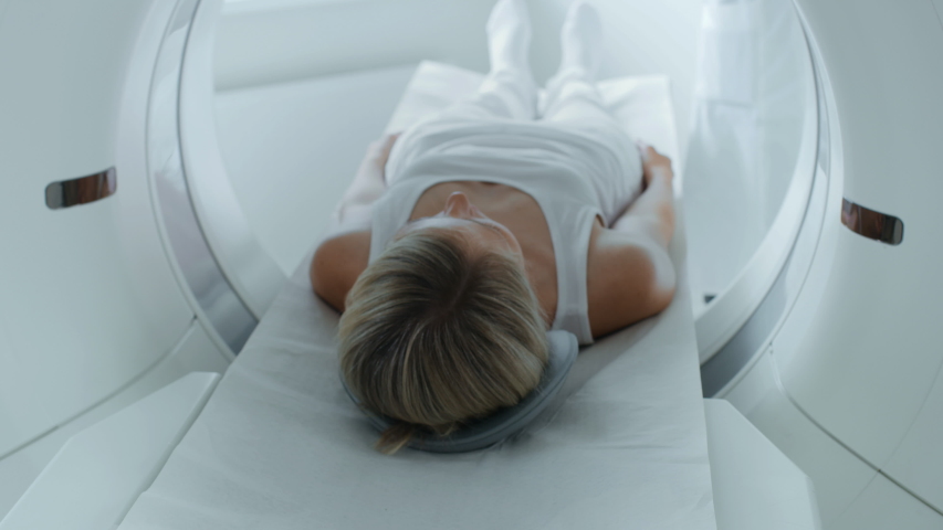 Female Patient Lying on CT or PET or MRI Scan Bed, Moving Inside the Machine While it Scans Her Brain and Vital Parameters. Augmented Reality Concept with VFX In Medical Lab with High-Tech Equipment. Royalty-Free Stock Footage #1048246471