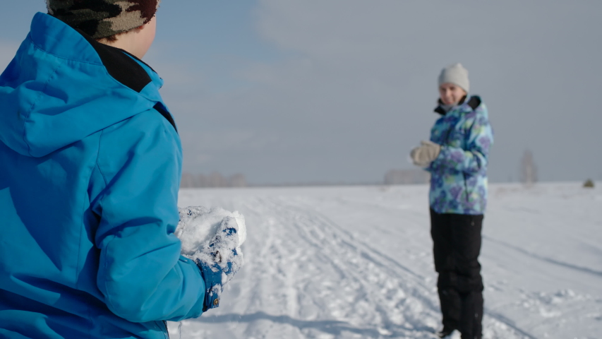 Happy family winter fun. Mother and her son play snowball fight. Slow motion.