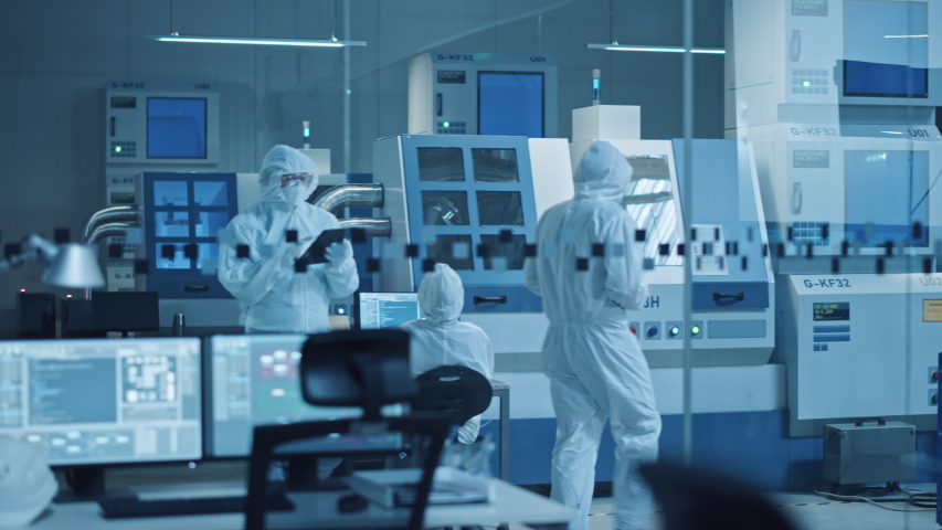 Research Factory Cleanroom: Engineer Wearing Coverall and Mask, Walking Through Workshopop Uses Tablet Computer. In Background Professionals Work on Modern High Tech CNC Machinery | Shutterstock HD Video #1048253908