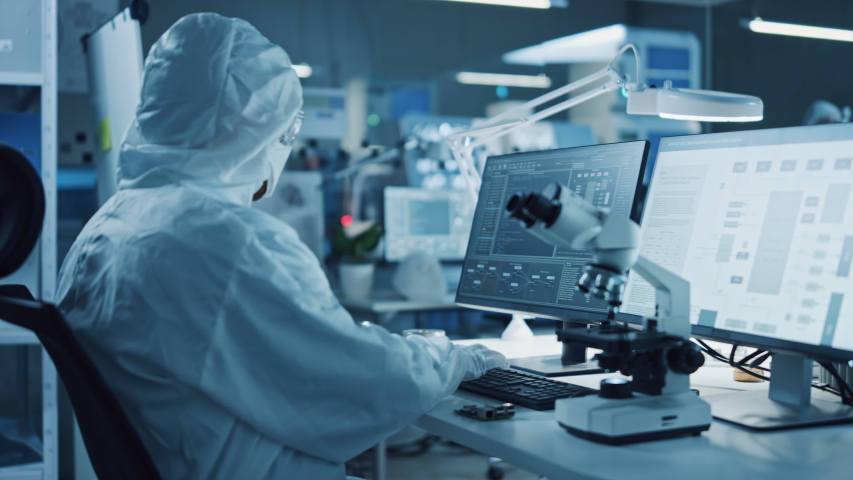 Modern Factory: Team of Engineers and Scientists in Clean Sterile Coveralls Work on Desktop Computers, Use Microscope, Developing Electronics for High-Tech Medical Electronics Research | Shutterstock HD Video #1048254007