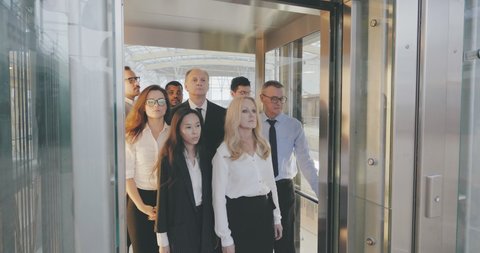 Crowd of diverse office employees entering glass elevator going out for lunch break. Business colleagues riding modern elevator. Coworkers walking in lift in office building