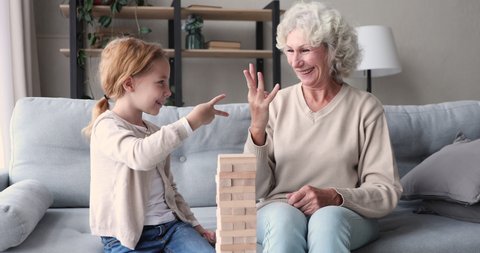 Happy senior grandma and cute kid granddaughter playing rock-paper-scissors hands build funny game at home. Two age generations family old grandparent and small grandkid enjoying activity together.