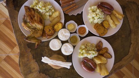 video looking from above of a variety of foods from a restaurant in the Peruvian jungle: chicken, chorizo, banana, yucca and salad. Accompanied with soft drinks from Quito