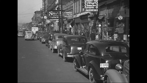 CIRCA 1938 - Footage is shot from a car as it drives past shops, restaurants, and movie theaters on a city street.