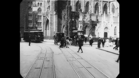 CIRCA 1911 - Pedestrians walk, and carriages and trolleys ride through the city streets of Manhattan, New York City.