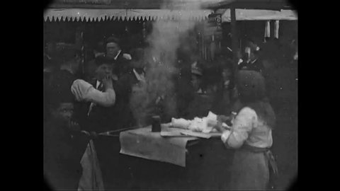 CIRCA 1902 - Carnival barkers are seen at work in a urban area of Hull, England, where people buy food and play games.