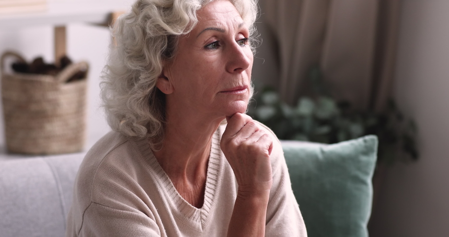 Pensive thoughtful senior grandma looking away thinking of solitude. Lonely sad older retired lady feeling melancholic sitting alone on sofa at home. Elder granny reflecting lost in thoughts concept Royalty-Free Stock Footage #1048270606