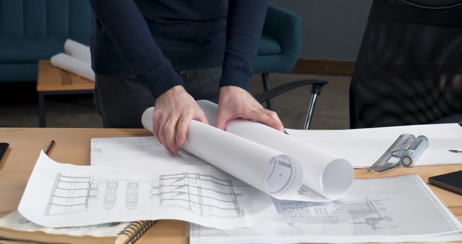 Close Up of young concentrated Architect Works with Blueprints, Sketches. Blueprints, Architects Tools Laying on His Desk. Workplace of an architect or designer, Bearded man in glasses makes Sketches. Royalty-Free Stock Footage #1048271044