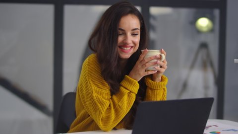 Closeup business woman looking laptop computer in home office. Smiling girl drinking tea near notebook indoor. Close up happy businesswoman smiling to laptop camera at remote workplace
