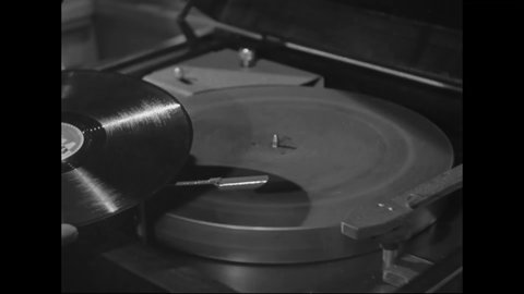 CIRCA 1940s - A man puts a record on a 78 rpm record player and plays it.