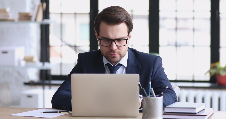 Angry stressed businessman wearing suit feeling mad about broken stuck laptop. Frustrated executive using computer outraged by financial market crash concept reads bad online news sits at office desk. Royalty-Free Stock Footage #1048278655