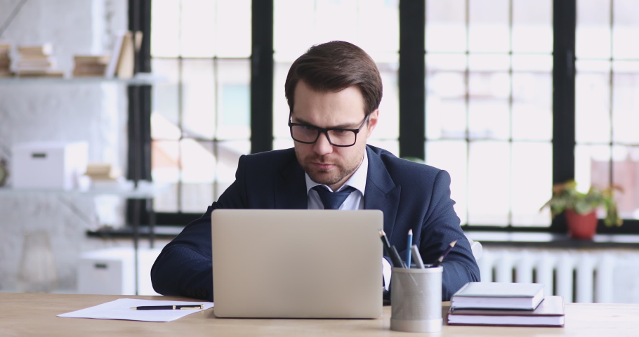 Excited male executive wears suit feels overjoyed looks at laptop. Happy motivated businessman investor winner using computer reads good news gets rewarded celebrates business success profit concept. Royalty-Free Stock Footage #1048278658