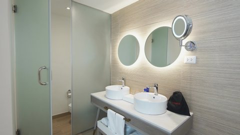 The hotel bathroom has a washbasin and a mirror. Mirror illumination in a modern interior. The new design of the toilet room vacation resort. Mirrors, washbasins, toilet and bathroom video.