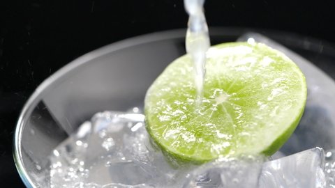 Pouring soda into a cocktail glass with lime and ice in slow motion on dark background, Close-up refreshing cold cocktail with lime