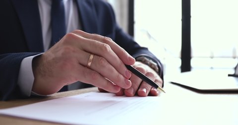 Businessman checking, signing legal document concept. Executive wearing suit reading financial contract, writing signature on official paper. Male hand holding pen doing paperwork, close up view