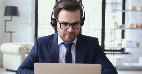 Male executive wears headset video calling on laptop. Businessman webinar speaker streaming live web training. Call center agent, service support manager speaking to distance customer in webcam chat.