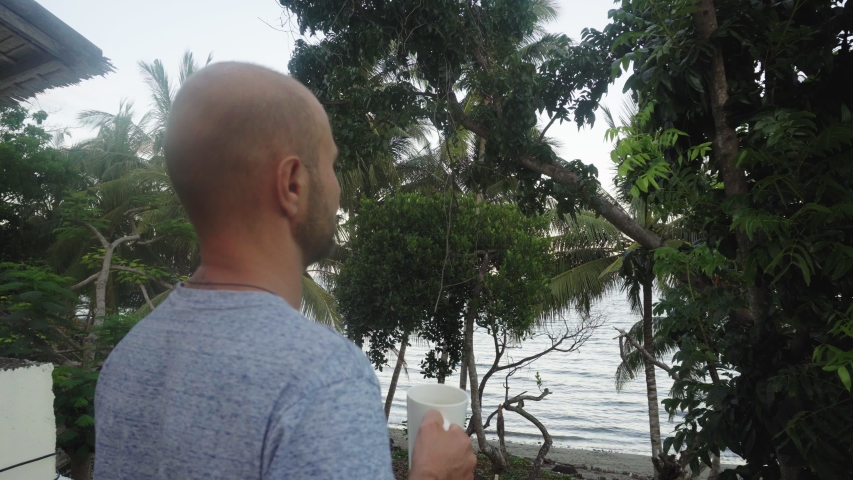 A young man drinks a hot drink on a background of beautiful tall palm trees.