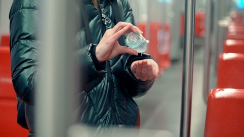 A young woman uses hand sanitizer liquid in a subway car, pandemic coronavirus concept
