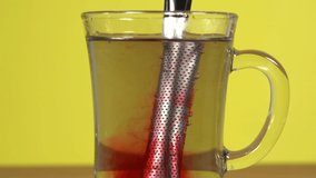 Closeup view video of transparent glass cup with silver long stick package with fruit tree inside. Mixing hot water with stick while making fresh tea.