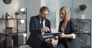 Male and female company workers in business suits holding documents while standing at modern office. Two partners working together on common financial project.