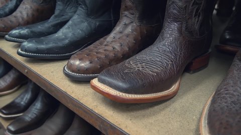 Cowboy boots in a store. Close-up of new cowboy boots on shelf. Aligned cowboys boots on a shelf in a store. Ostrich and crocodile leather cowboy boots lined up in a row in a retail store.