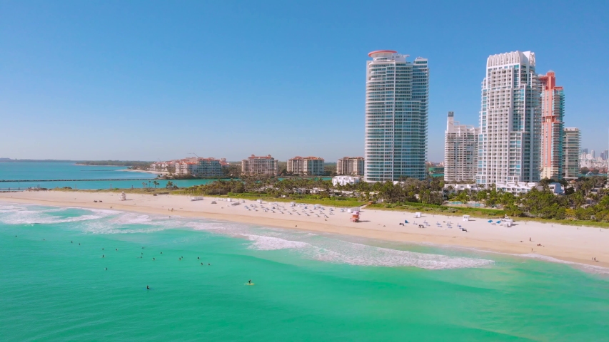 Drone flying forward near Miami Beach, South Beach, Florida. Cinematic video of a luxury resort in Miami South Beach. Surfers ride surfs in the ocean waves. Miami Beach on a sunny day, aerial view