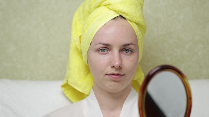 A girl with a towel on her head looks in the mirror and smears face with cosmetic cream. Natural cosmetic concept. Skin care, acne treatment, moisturizing skin.