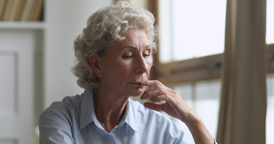 Thoughtful middle aged hoary woman feeling lonely at home, head shot close up. Unhappy mature granny thinking of health problems bad diagnosis. Lost in thoughts sad grandma suffering from depression. Royalty-Free Stock Footage #1048318054