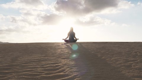SLOW MOTION Gimbal moving in wide to close up shot of woman in yoga pose with crossed legs shot from behind. Relaxation and meditation in the desert. Summer sunset in desert.